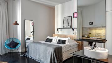 Une chambre d’hôtel moderne avec un grand lit, une table de chevet dotée d’un lavabo blanc, un miroir et une vue sur la salle de bain.