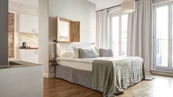 A bedroom with a bed, a bedside table, a mirror, a window with curtains, and a view of the city.