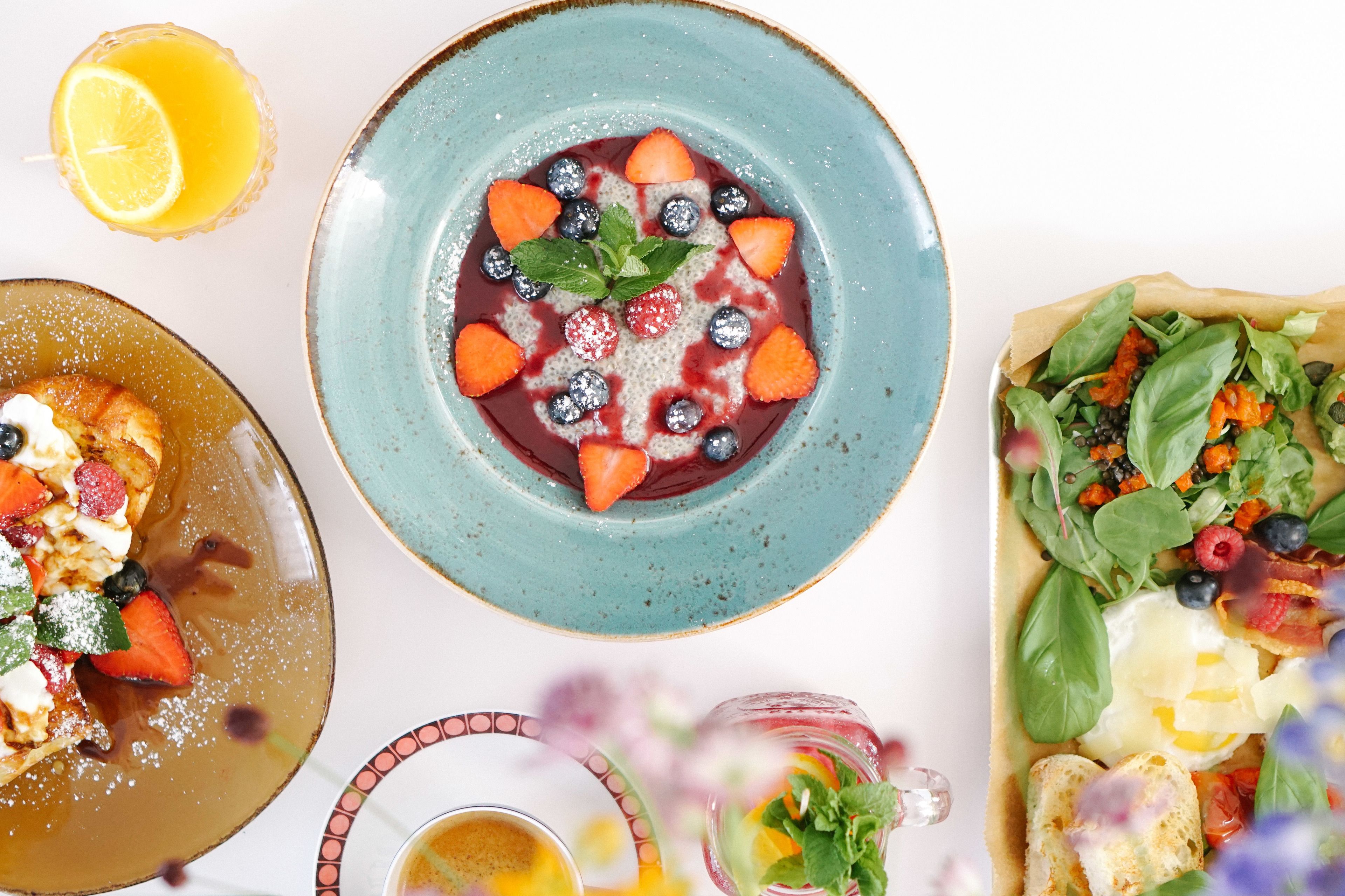 A variety of dishes including a bowl of berries and strawberries, a plate of scrambled eggs, and a salad with greens and tomatoes.