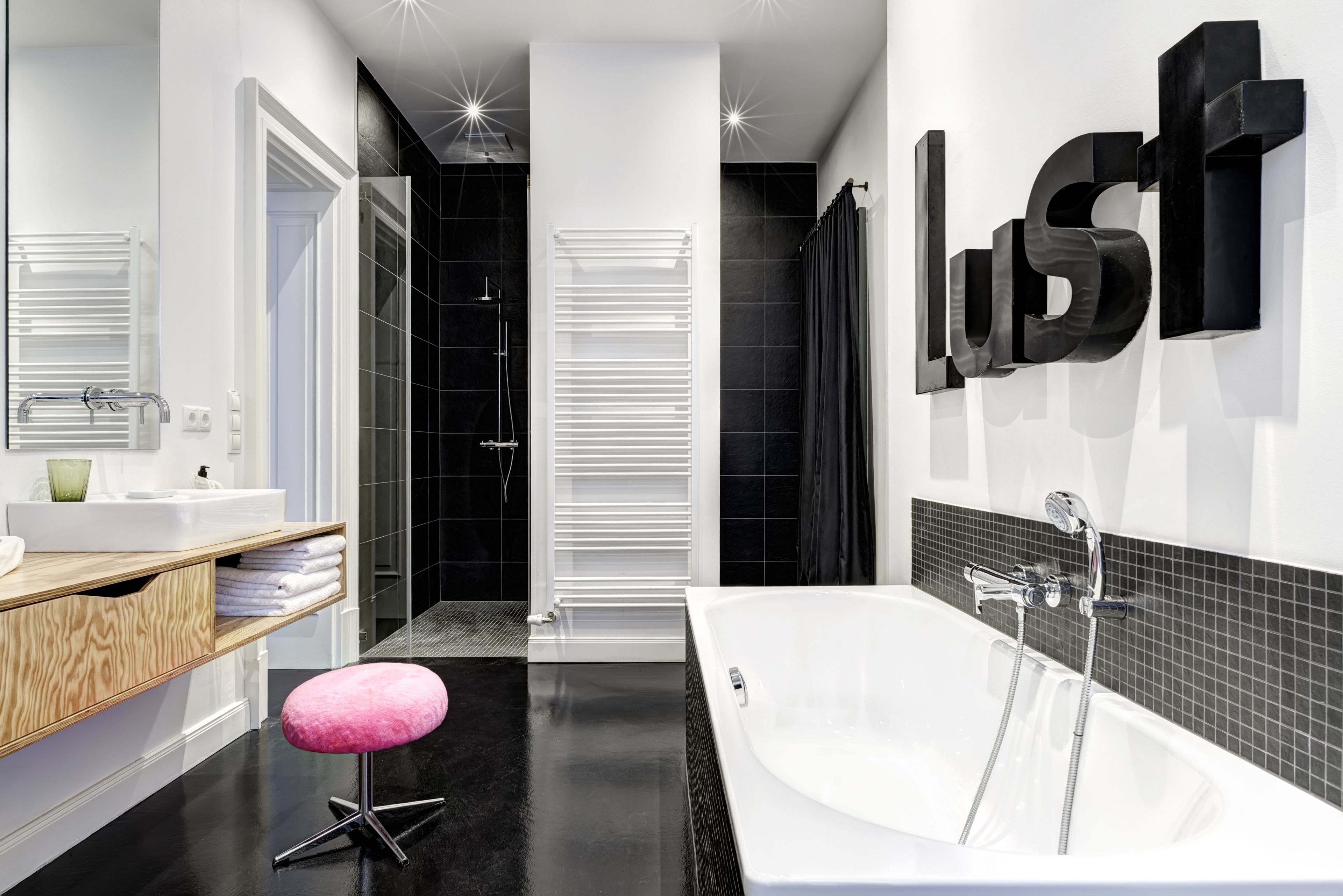 Un baño moderno con una bañera blanca, paredes de azulejos negros y un mueble de tocador de madera.