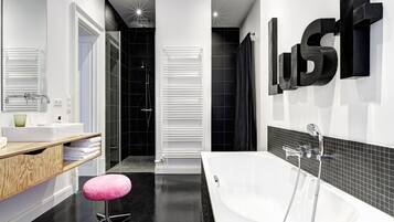 A modern bathroom with a white bathtub, black tiled walls, and a wooden vanity.
