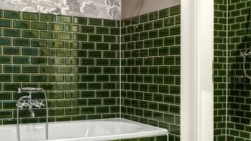 A bathroom with a large bathtub, green mosaic tiles, a white sink, and a shower area.