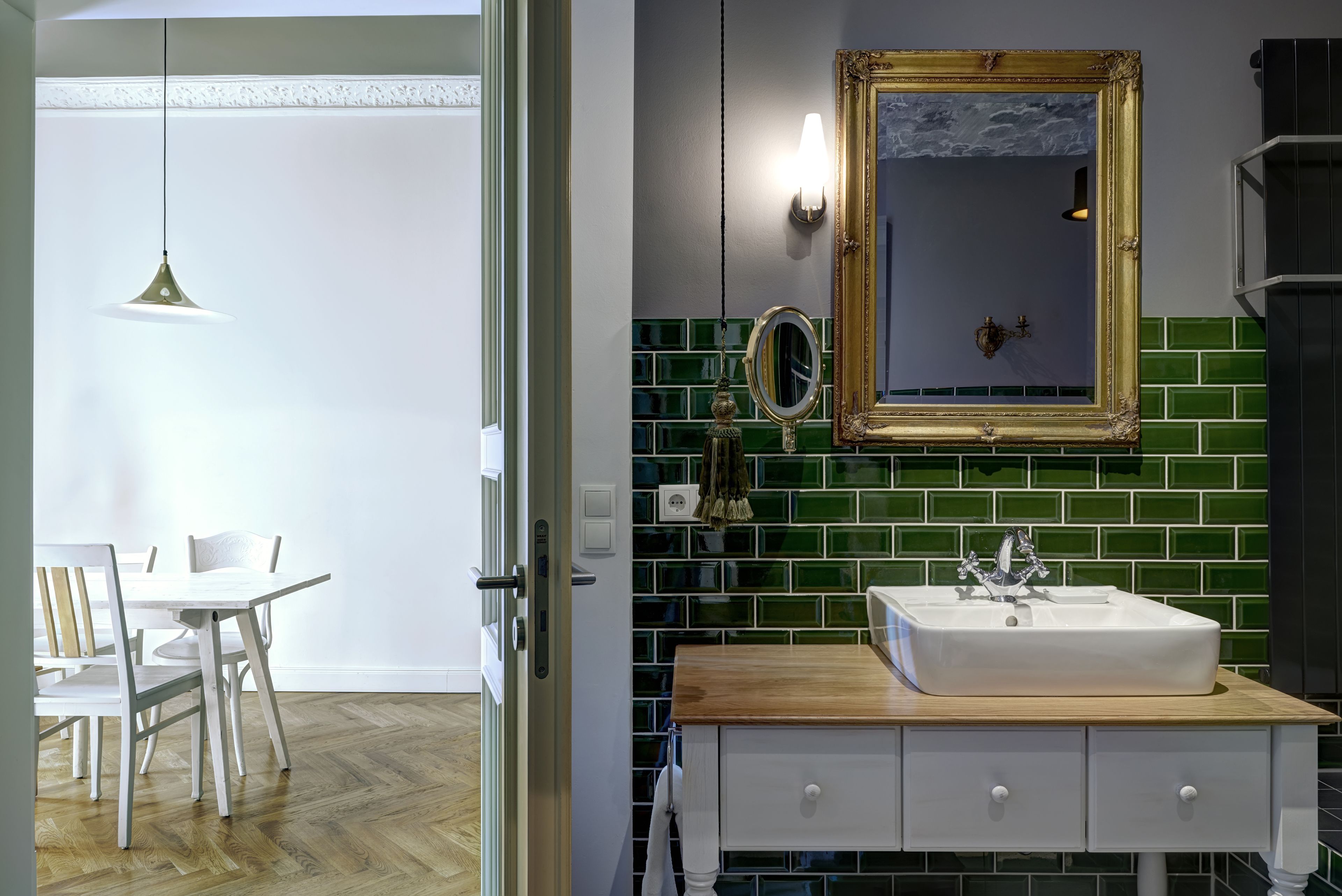 A bathroom with a white sink, green mosaic tiles, a gold-framed mirror, and a hanging pendant light.