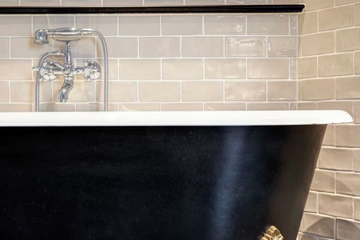 Une baignoire noire, dotée d’un robinet et d’une pomme de douche en chrome, placée devant un mur carrelé.