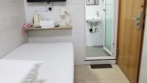 Une chambre d’hôtel comprenant un lit, une table de chevet avec un téléphone et un sèche-cheveux, un téléviseur fixé au mur, une salle de bain avec un lavabo et un miroir, et une porte donnant sur une autre pièce.