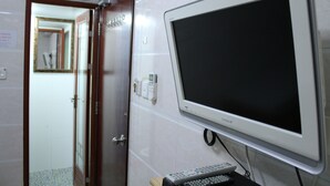 Une pièce avec un téléviseur fixé au mur, une porte donnant sur une autre pièce et une petite table sur laquelle se trouve une télécommande.