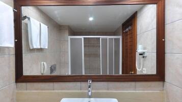 Un baño con un espejo grande, un lavamanos blanco y una zona de ducha.