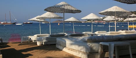 Een privéstrand, ligstoelen aan het strand, parasols, een strandbar