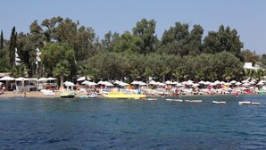 A beach with umbrellas, boats, and people. - Okaliptus Hotel (Bodrum)