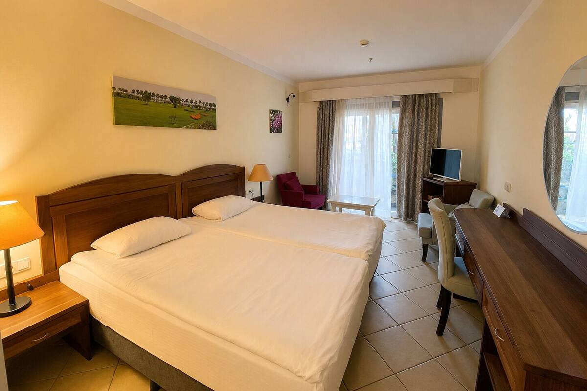 A hotel room with a large bed, a desk, a chair, a TV, and a window with curtains.