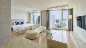 Une chambre d’hôtel moderne avec un grand lit, un canapé, une table basse en verre et un téléviseur.