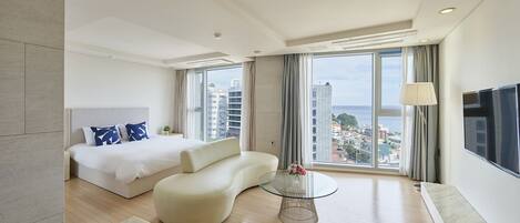 A modern hotel room with a large bed, a sofa, a glass coffee table, and a TV.