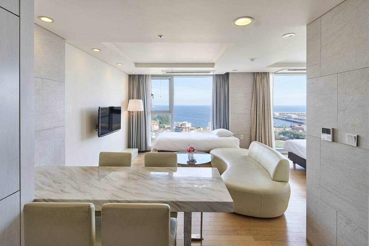 A modern hotel room with a large bed, a seating area with a table, and a TV mounted on the wall.
