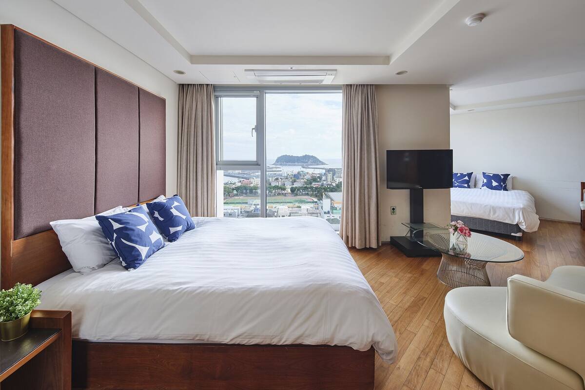 A hotel room with a large bed, a TV, a sofa, and a view of a cityscape.