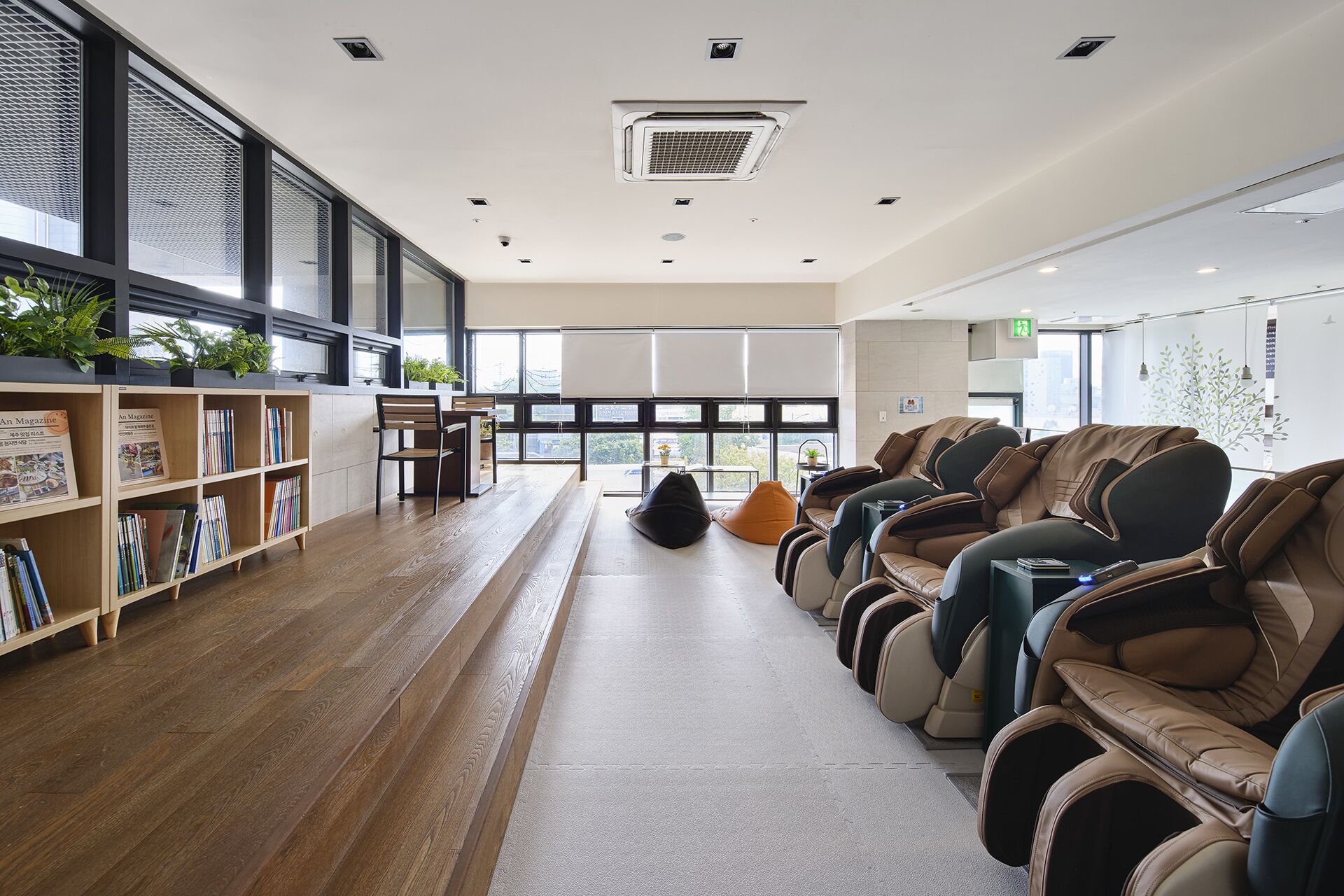 A modern library with bookshelves, a reading area, massage chairs, and large windows.