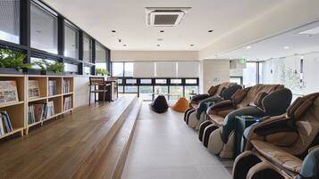 Een moderne bibliotheek met boekenrekken, een leeshoek, massagestoelen en grote ramen.