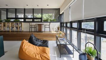 Un espace de vie moderne doté d’une grande fenêtre, d’un coin salon avec un fauteuil poire, d’une petite table avec une plante et d’une bibliothèque.