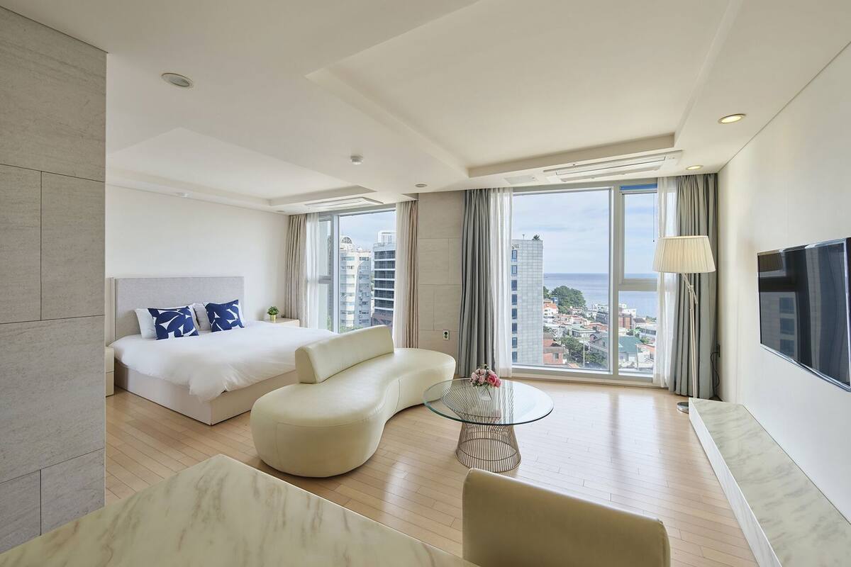 A modern hotel room with a bed, sofa, glass coffee table, and a TV.