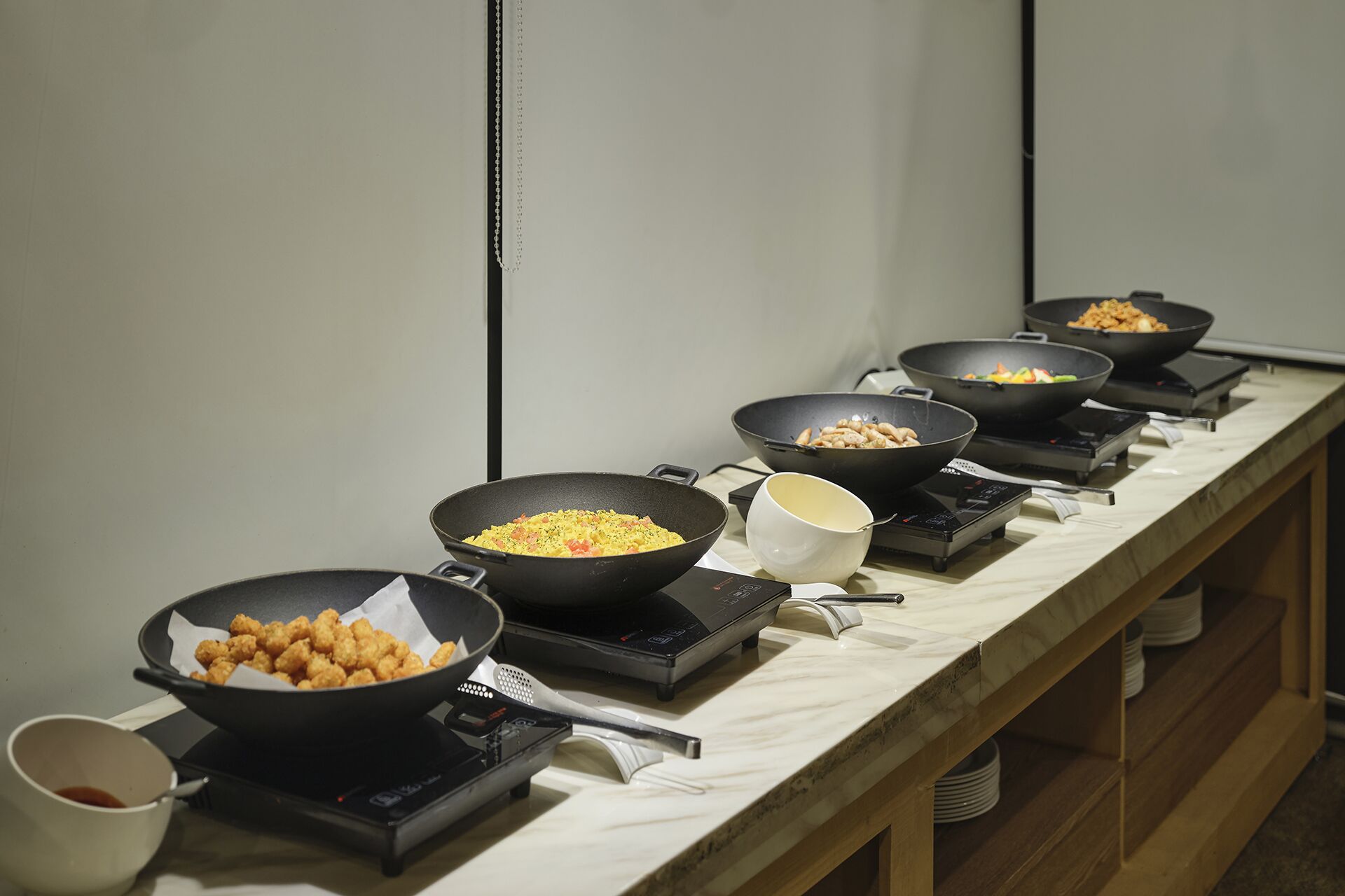 A kitchen counter with multiple electric skillets and a white mug.