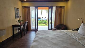 A hotel room with a large bed, a desk with a chair, a small table, and a view of the outdoors.