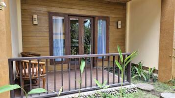 A wooden balcony with a railing, a chair, and a small garden area with plants and a stone wall.