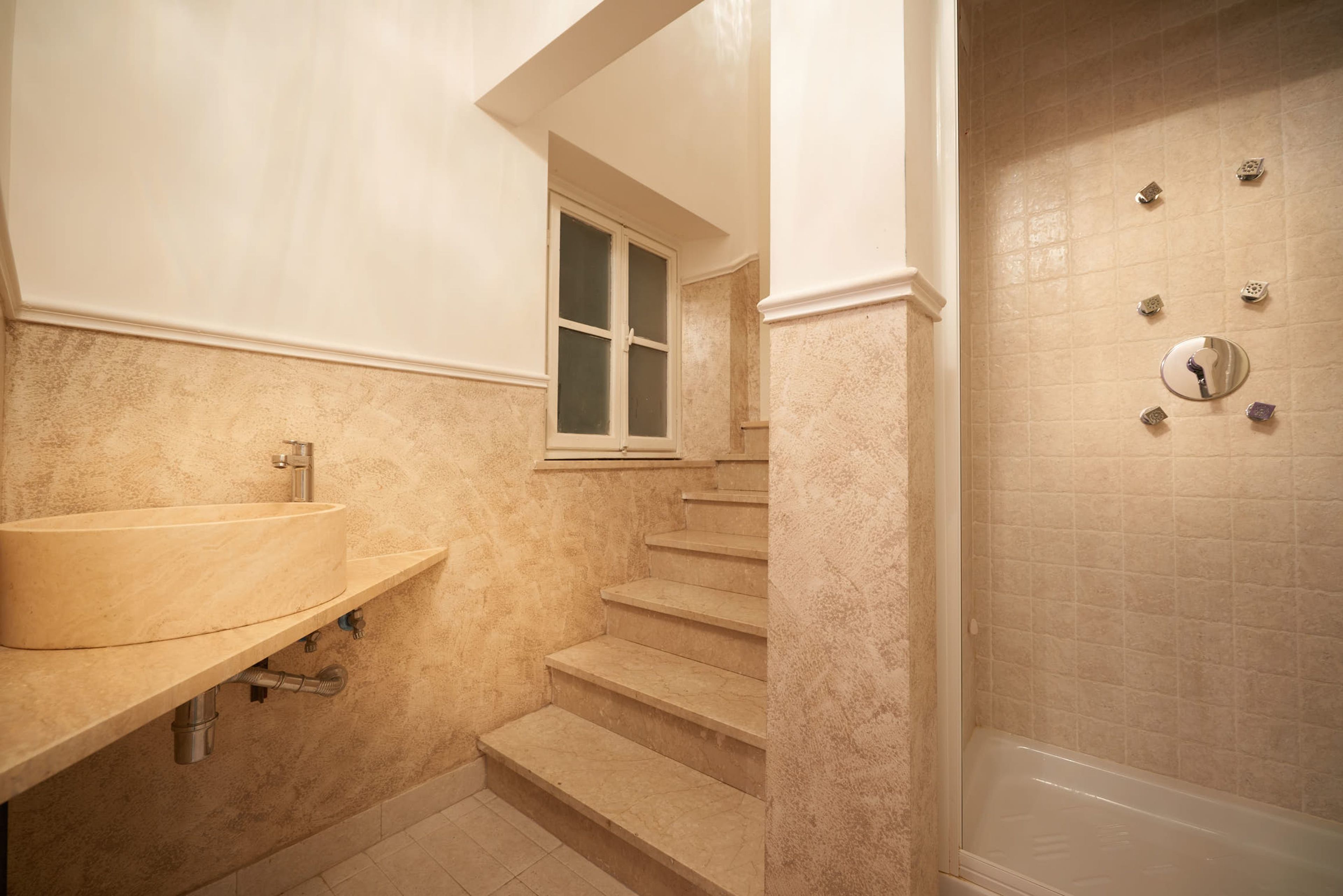 A bathroom with a beige sink, a window, and a shower area.