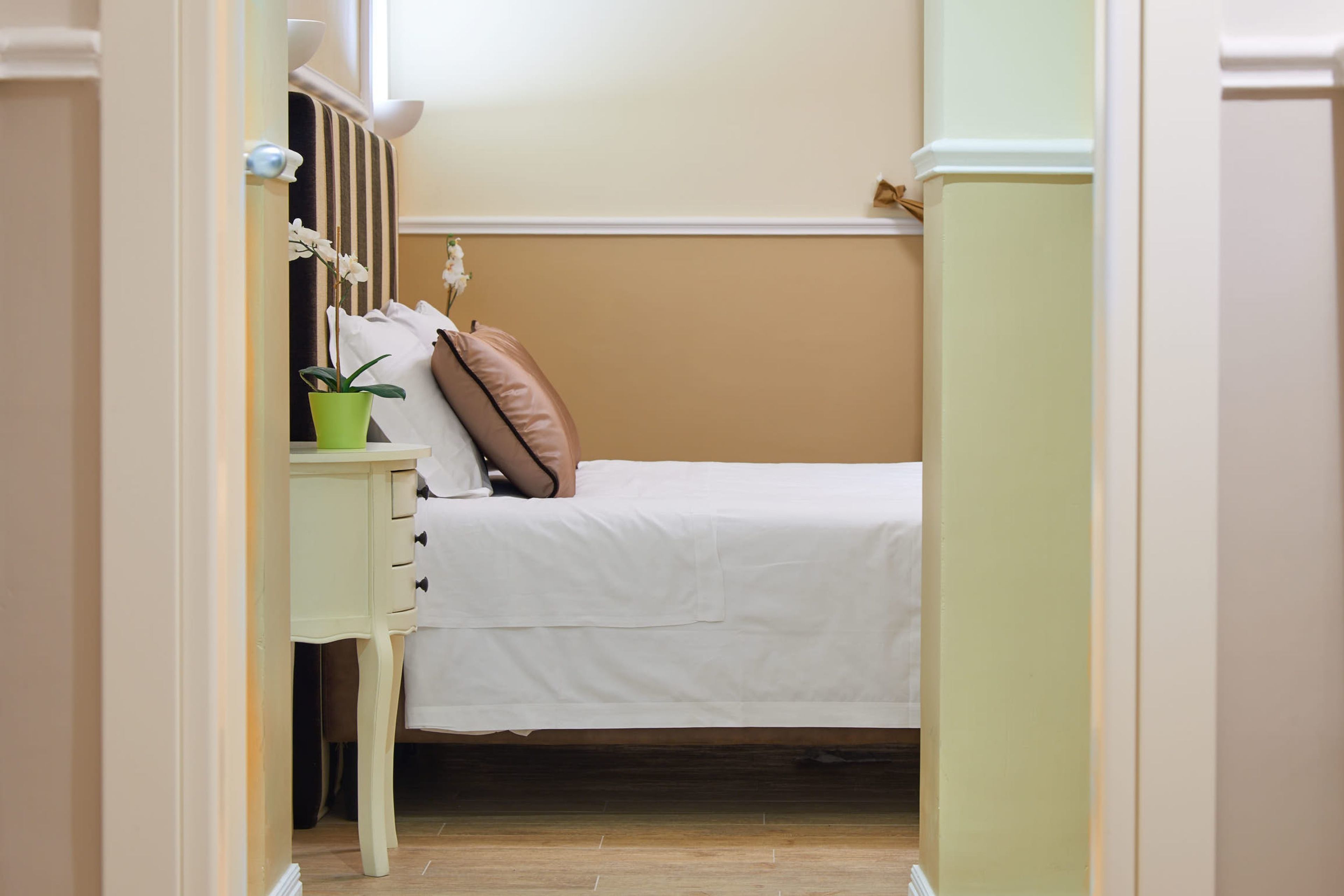 Een slaapkamer met een bed, nachtkastje, een groene plant en een bruin kussen.