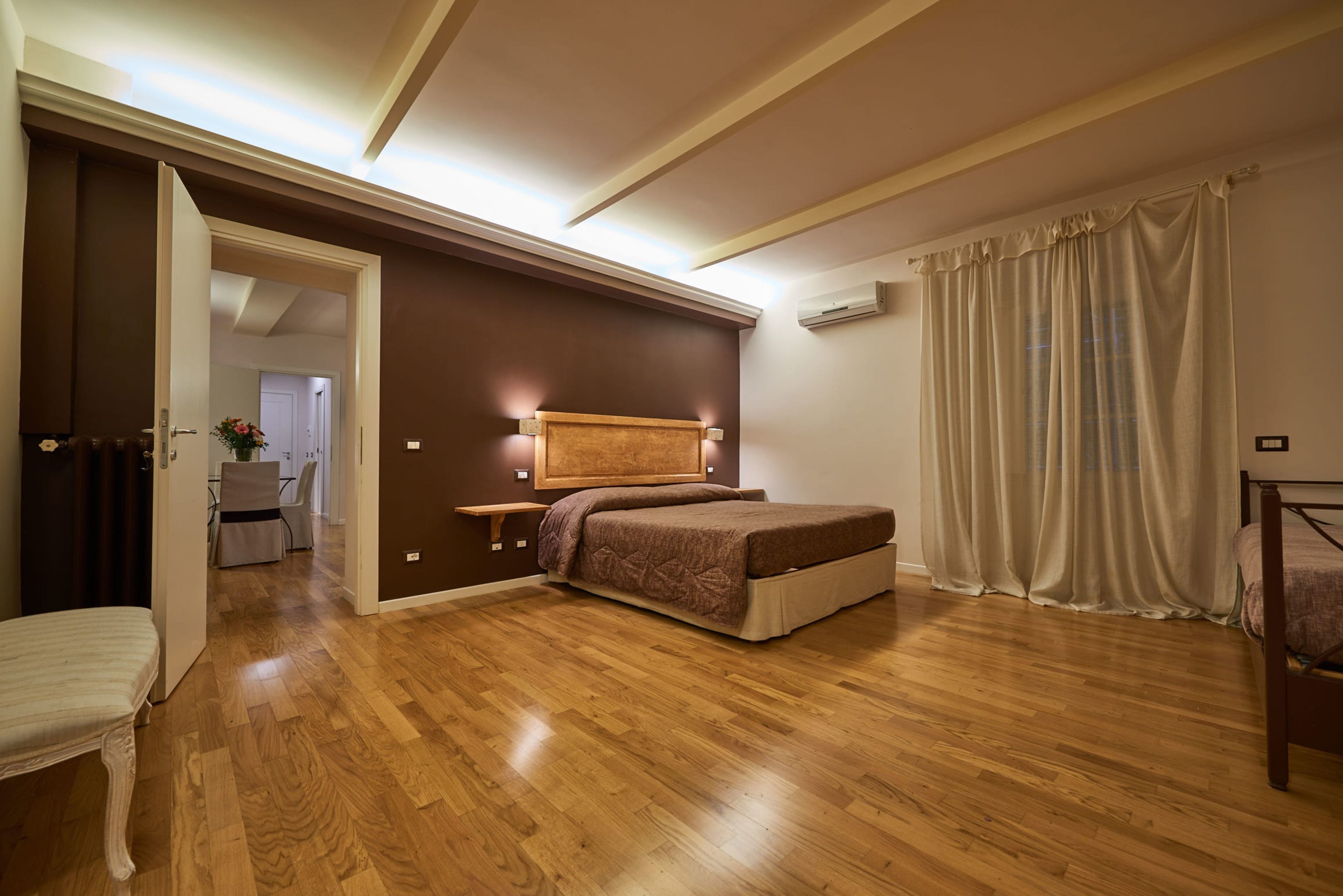 Ein Schlafzimmer mit Holzboden, einem Bett mit Kopfteil, einem Nachttisch und einem Fenster mit Vorhängen.