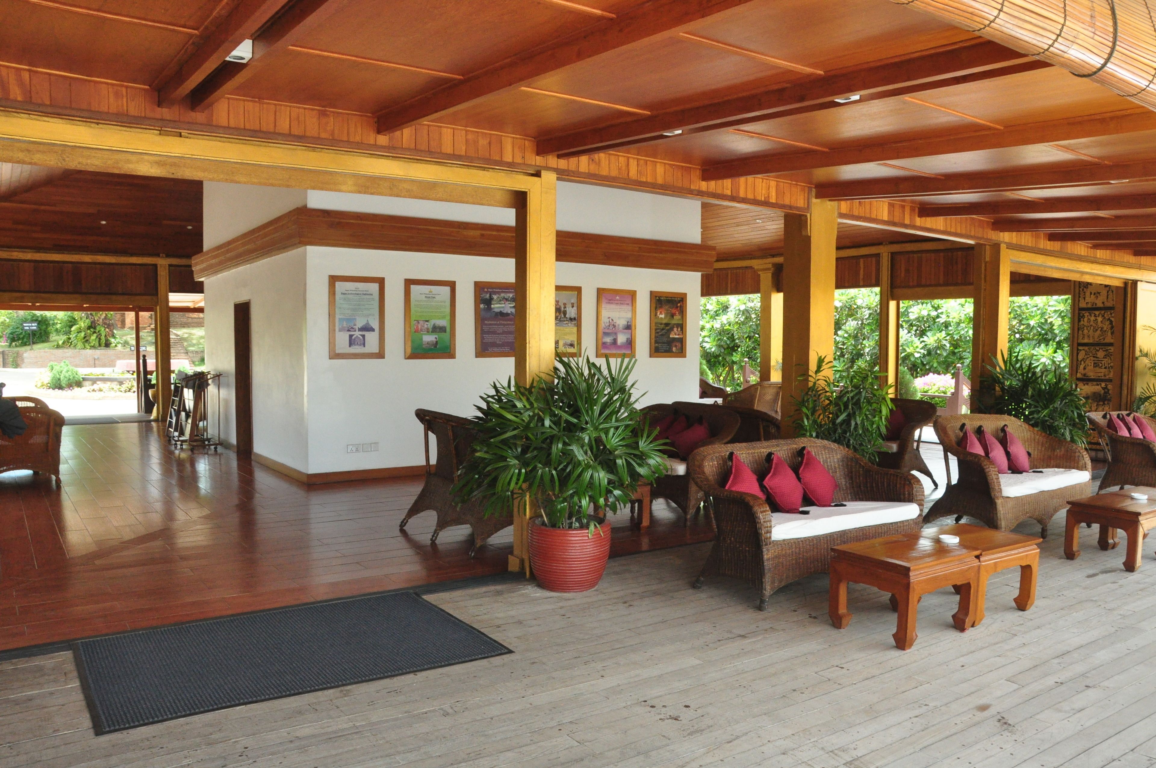A spacious lobby with wooden flooring, wicker furniture, and a large potted plant.