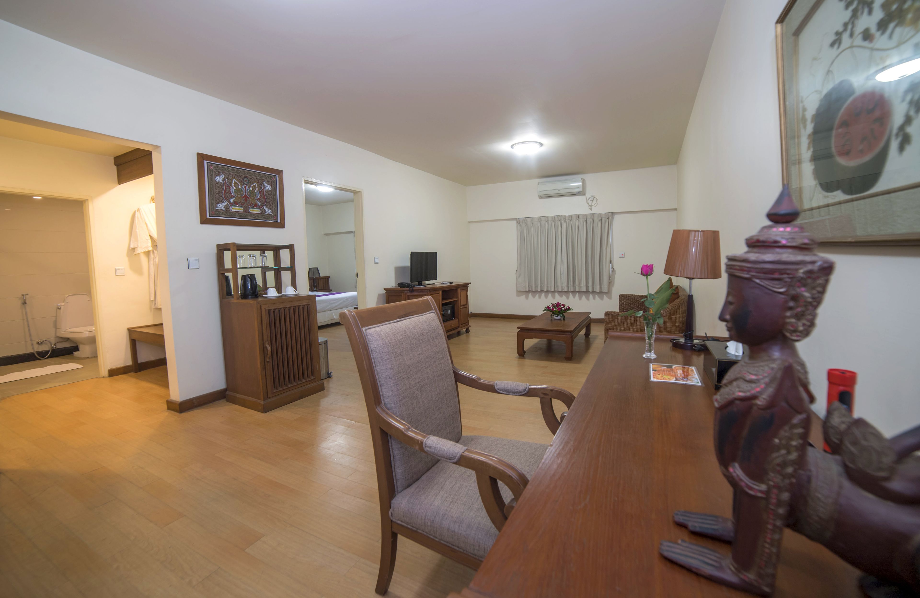 A spacious living room with a wooden dining table, a comfortable armchair, a television, and a decorative statue.