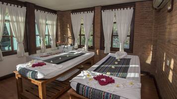 Relax in a serene spa room with two massage tables, a bathtub, and large windows.