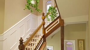 A grand staircase with a wooden handrail, white balusters, and a red patterned carpet. - Victoria's Mansion Guest House (Toronto)