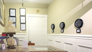 A reception area with a marble counter, framed certificates on the wall, and clocks labeled with city names. - Victoria's Mansion Guest House (Toronto)