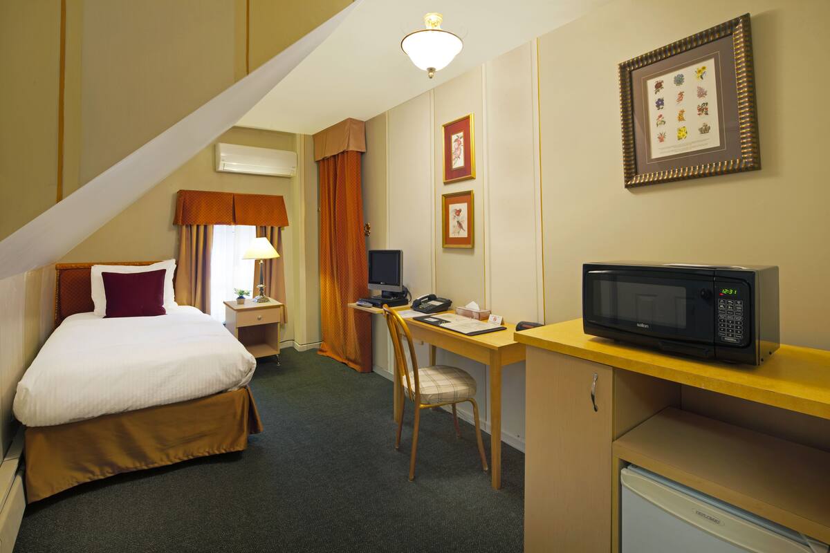 A hotel room with a bed, desk, chair, microwave, and a small refrigerator.