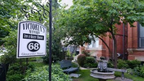 A sign for Victoria's Mansion Inn & Guest House on Gloucester Street, surrounded by greenery and a fountain. - Victoria's Mansion Guest House (Toronto)