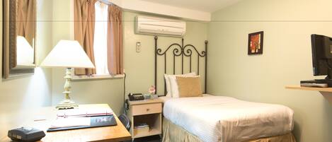 A hotel room with a bed, bedside table, lamp, desk, and a television.