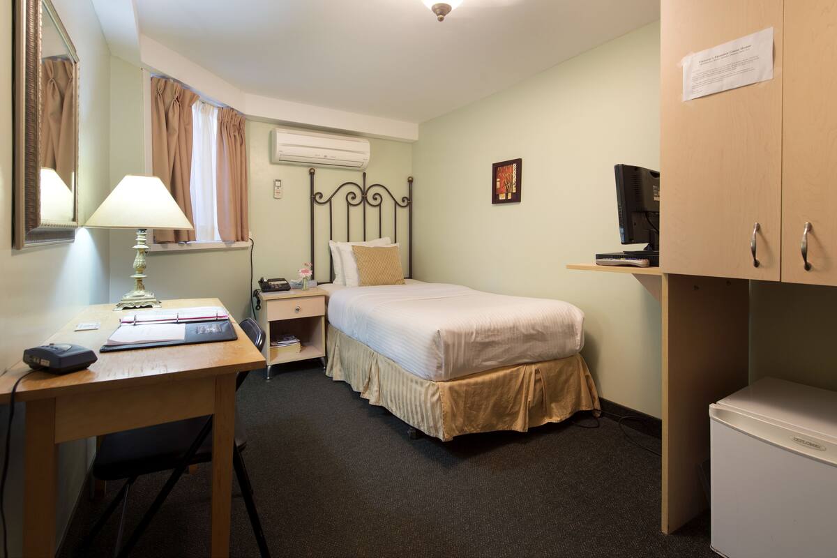 A hotel room with a bed, desk, chair, lamp, and a small refrigerator.