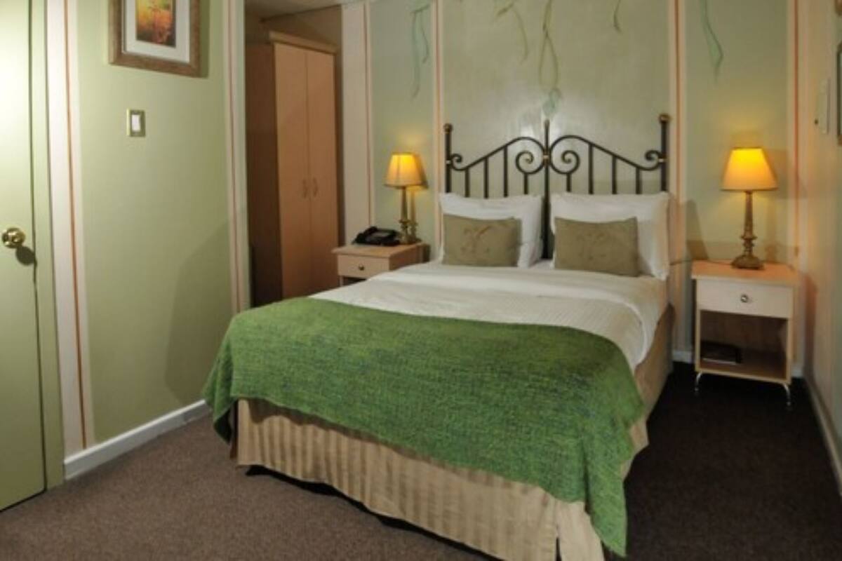 A neatly made bed with a green blanket, two bedside lamps, and a wooden nightstand.