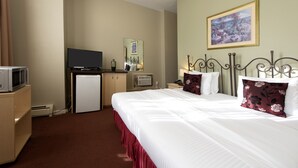 A hotel room with a large bed, a television, a desk with a computer, and a painting on the wall. - Victoria's Mansion Guest House (Toronto)