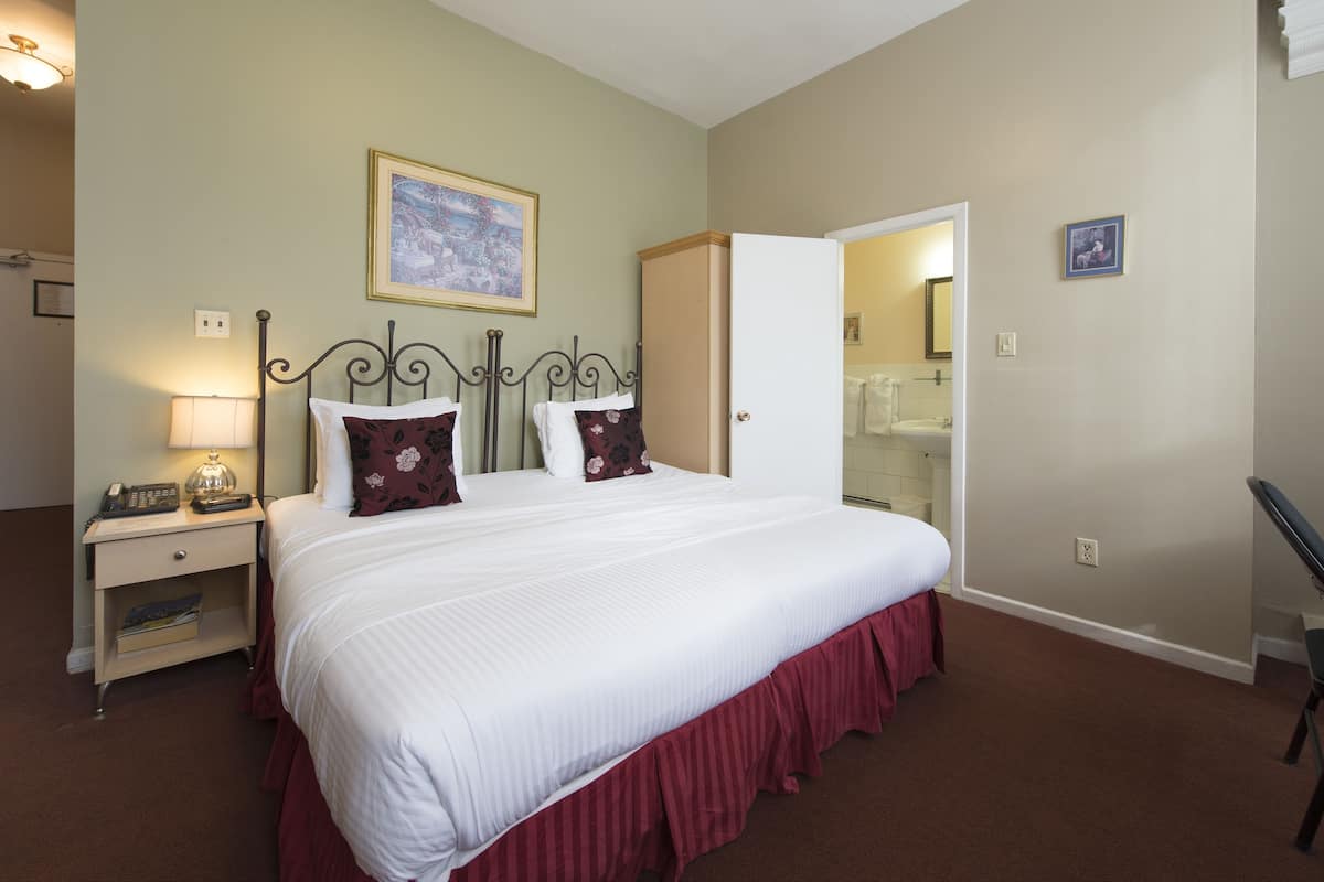 A neatly made bed with a white comforter and red skirt, a bedside lamp, and a nightstand with a telephone and book.