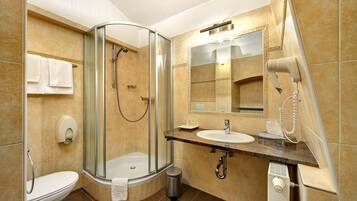 A modern bathroom with a glass-enclosed shower, a toilet, a sink, and a hairdryer mounted on the wall.