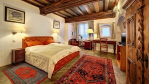 A bedroom with a wooden ceiling, a bed with white bedding, two lamps, a desk with a chair, and a television. - Hotel Konvice (Cesky Krumlov)