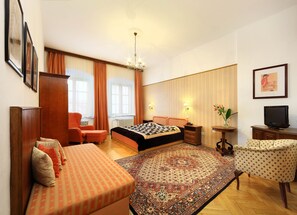 A hotel room with a bed, a sofa, a chair, a television, and a carpet. - Hotel Konvice (Cesky Krumlov)