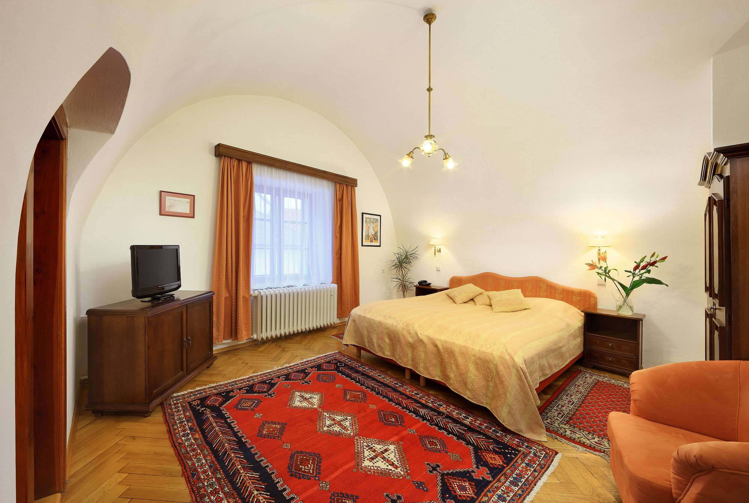 A bedroom with a bed, a television on a cabinet, a rug, and a chair.
