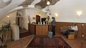 A reception area with a wooden reception desk, a patterned rug, and a seating area with a sofa and a chair. - Hotel Konvice (Cesky Krumlov)
