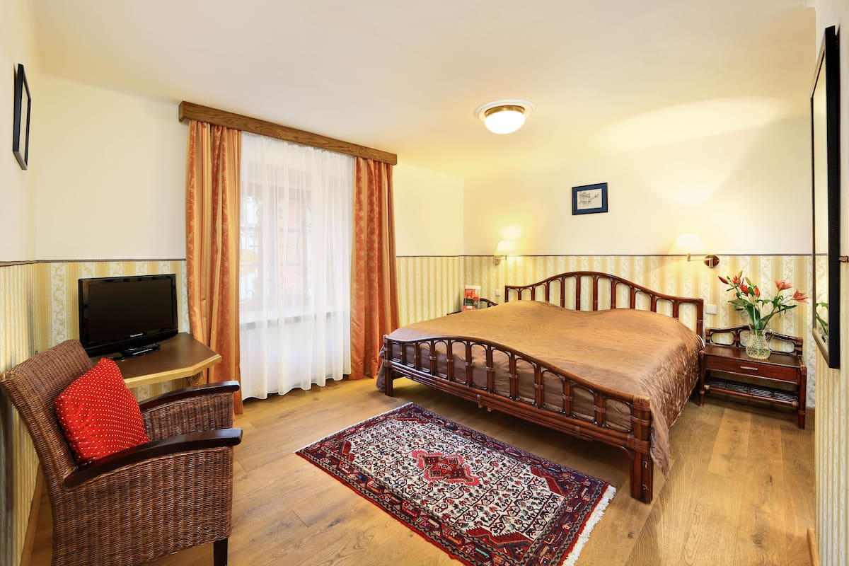 A hotel room with a bed, a TV, a wicker chair, a rug, and a bedside table with a vase of flowers.