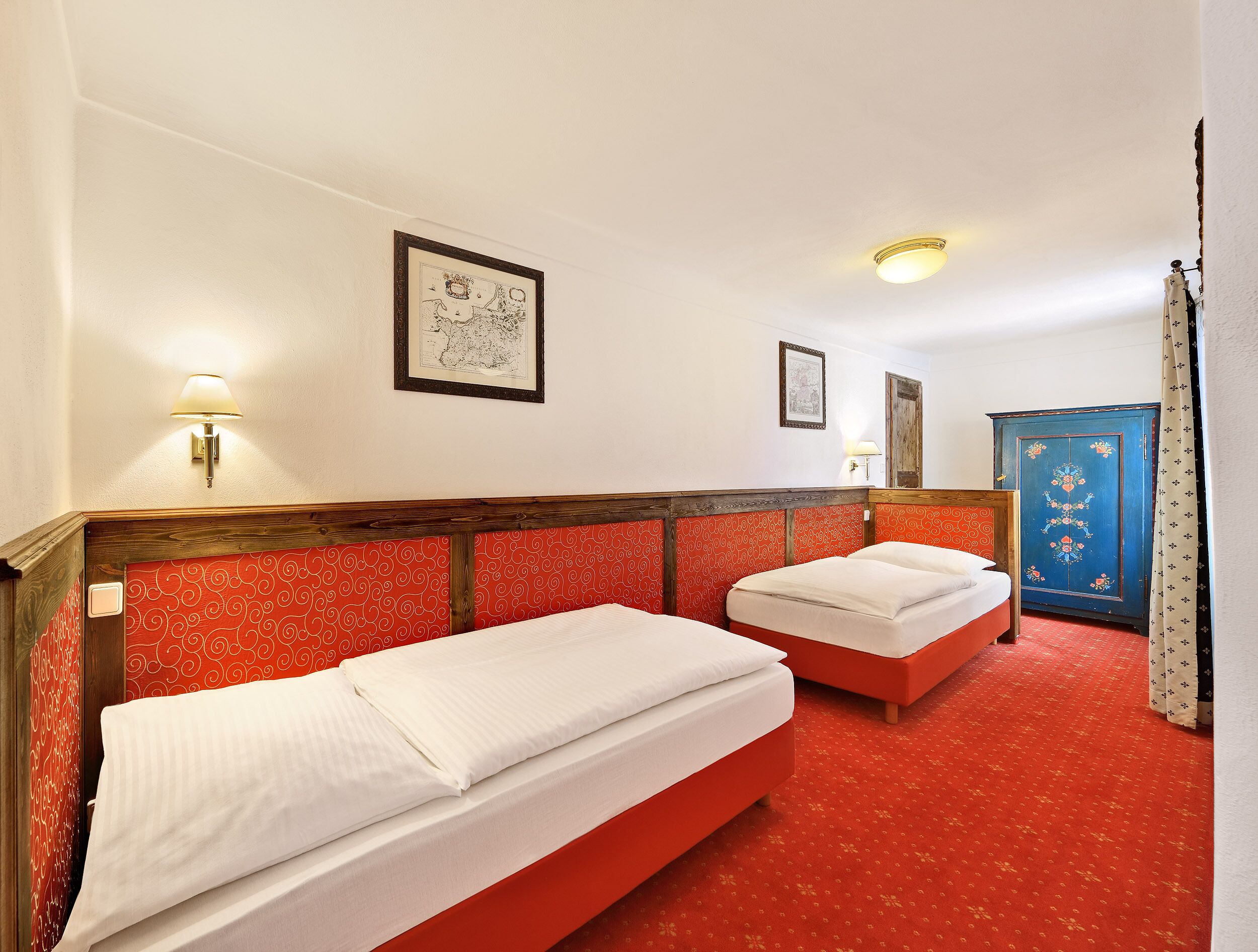 A hotel room with two beds, a red patterned wall, a wooden headboard, and a blue door with floral decorations.