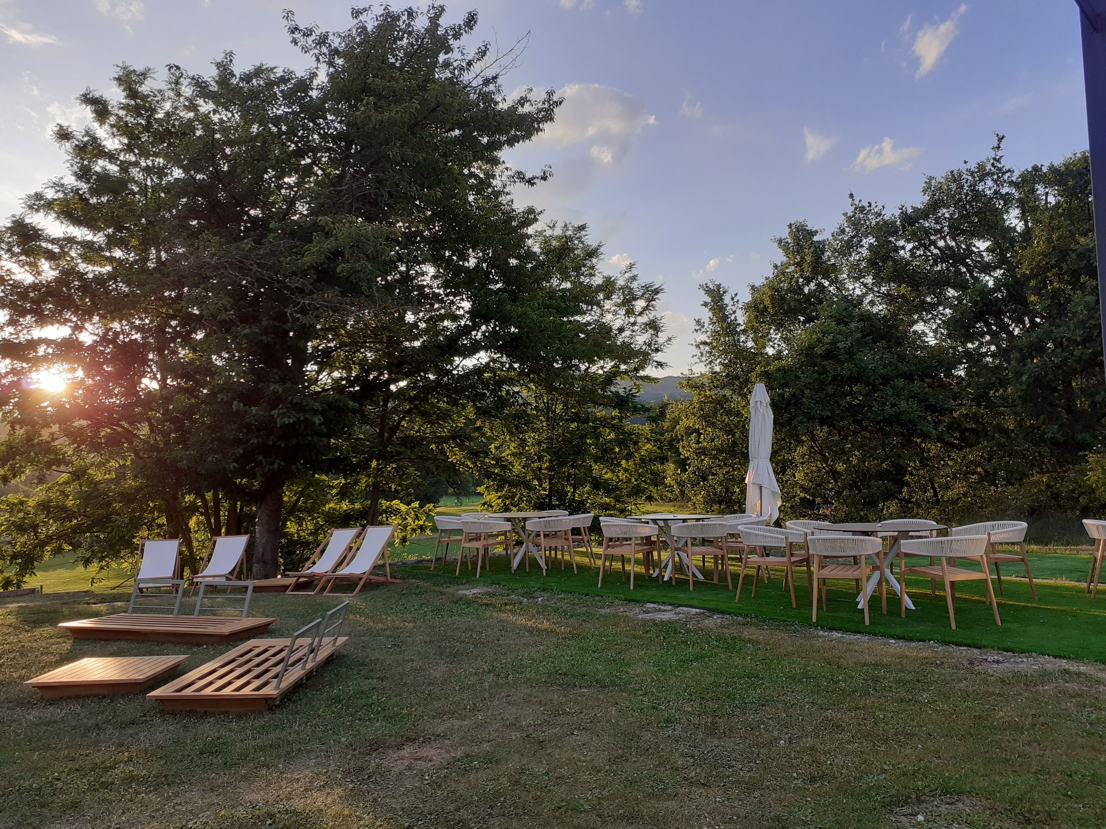 Un espacio al aire libre con sillones de descanso y mesas, rodeado de árboles y vistas del paisaje.