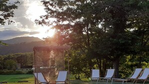 A serene outdoor setting with wooden lounge chairs and a pergola, surrounded by lush greenery and a backdrop of hills. - Golf Resort de Digne by Adonis (Digne-les-Bains)