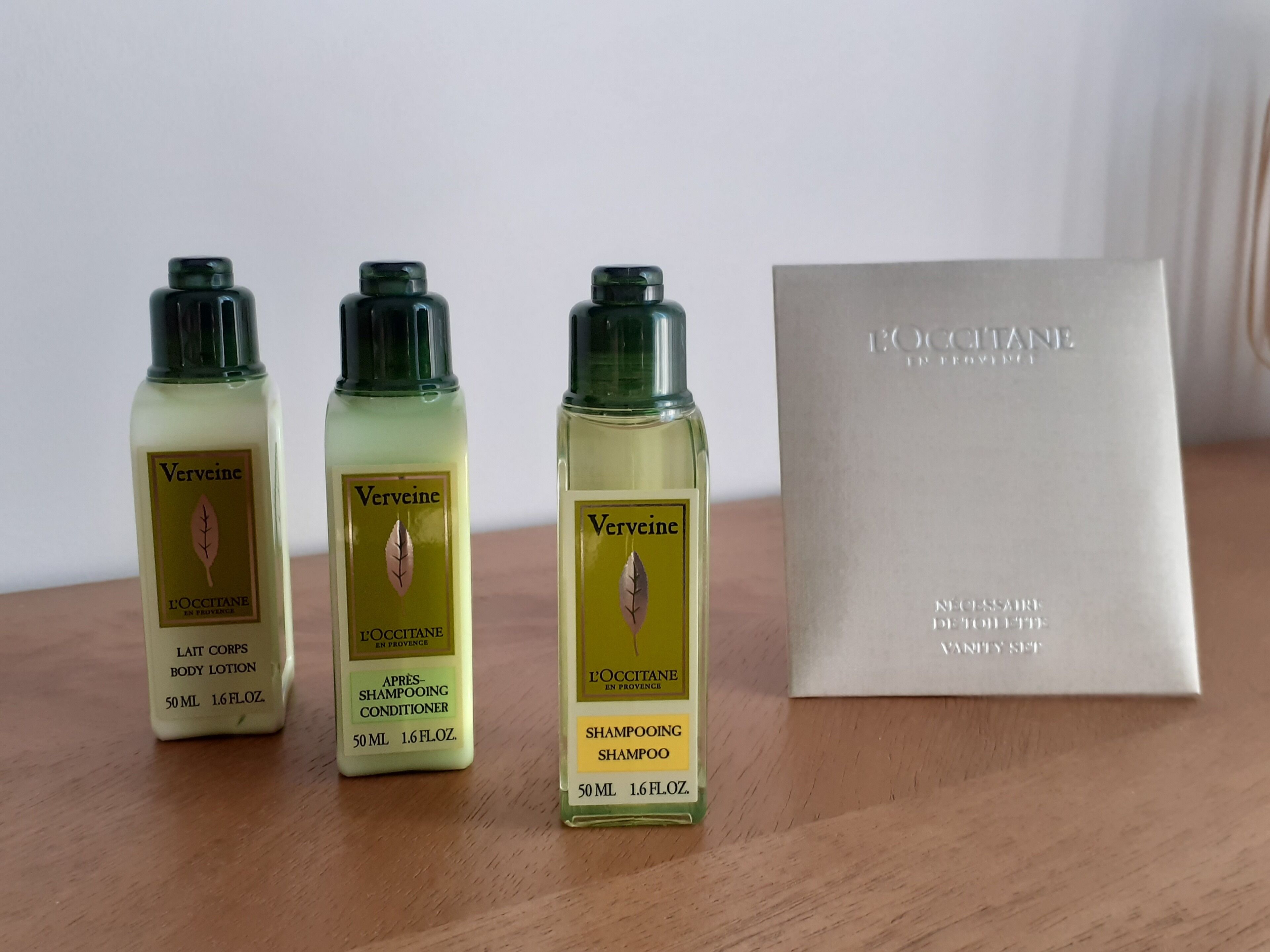 Tres botellas de loción corporal Vervine, una botella de champú Vervine y una caja de set de artículos de aseo Vervine sobre una superficie de madera.